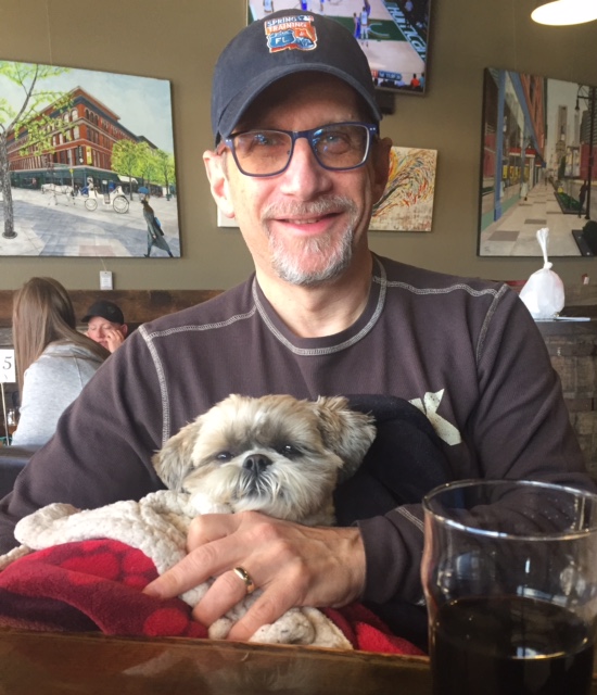 A man with glasses and a ball cap holds his dog, a shih-tzu. Ken is an ambassador for the great candy run!